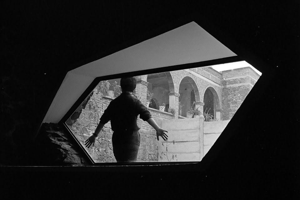 Silueta de una persona frente a una ventana angular, con el patio arqueado de la casa al fondo